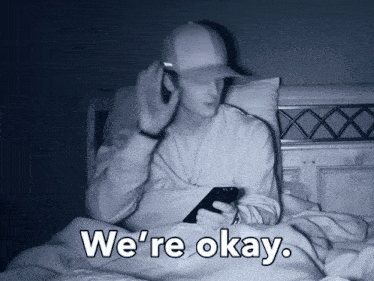 a man laying on a bed with a cell phone and the words we 're okay