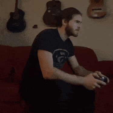a man in a blue shirt is sitting on a red couch playing a video game