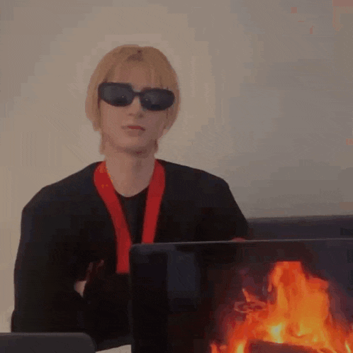 a man wearing sunglasses and a red scarf is sitting in front of a laptop computer with flames coming out of it .