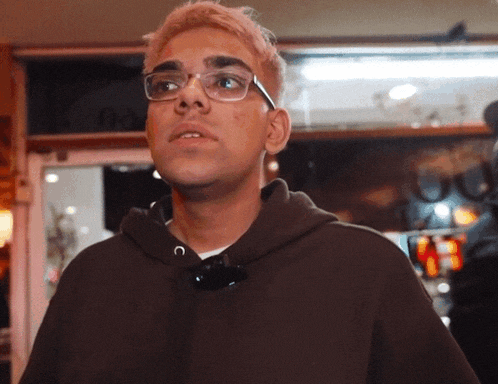 a man wearing glasses and a brown hoodie stands in front of a door that says box