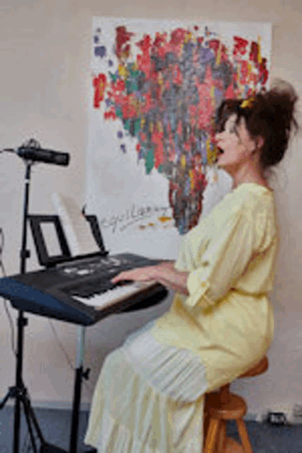 a woman in a yellow dress is sitting on a stool playing a keyboard in front of a microphone .