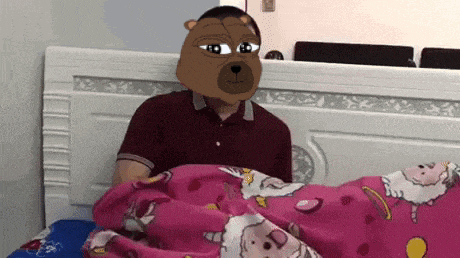 a man with a teddy bear mask on his head is laying in bed with a pink blanket .