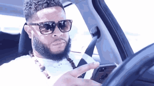 a man wearing sunglasses and a necklace is sitting in a car