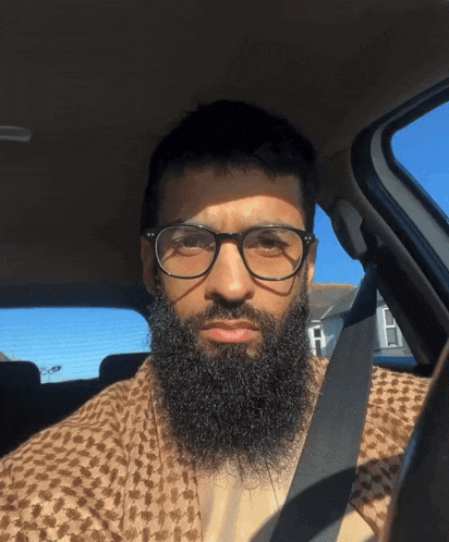 a man with a beard wears glasses and a seat belt