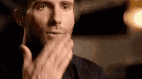 a close up of a man covering his mouth with his hand and looking at the camera .