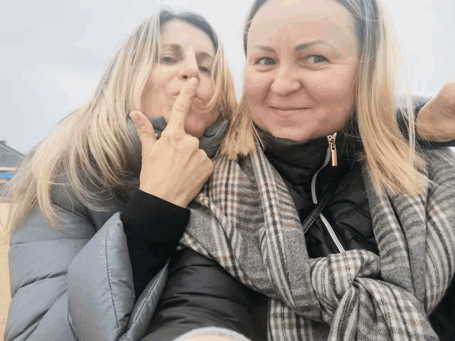 two women are posing for a picture and one has her finger on her mouth