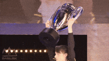 a person holding a trophy in front of a basilisk sign