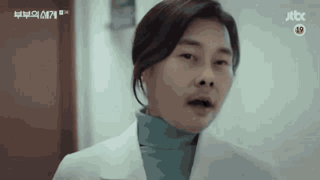 a man wearing a white coat and a green turtleneck is making a funny face .