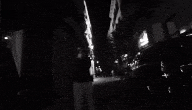a black and white photo of a person walking down a street at night