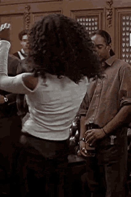 a woman with curly hair is dancing in a room while a man stands behind her .