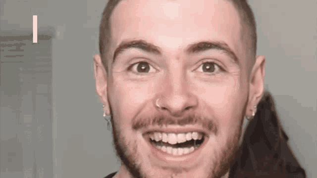 a close up of a man 's face with a nose ring and earrings smiling .