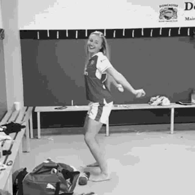 a woman in a soccer uniform is dancing in a locker room .