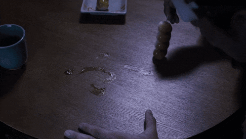 a person 's hand is on a wooden table with a cup of coffee