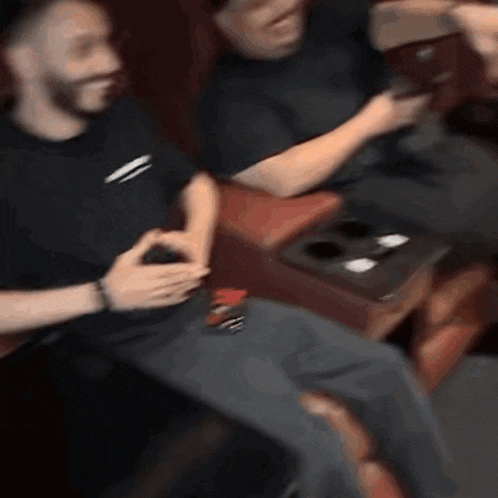 two men are sitting in a movie theater watching a movie and one of them is holding a cell phone .