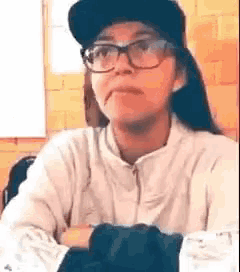 a woman wearing a hat and glasses is sitting at a table with her arms crossed .