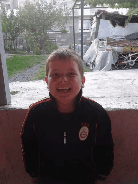 a young boy wearing a jacket that says ' galatasaray ' on it smiles for the camera