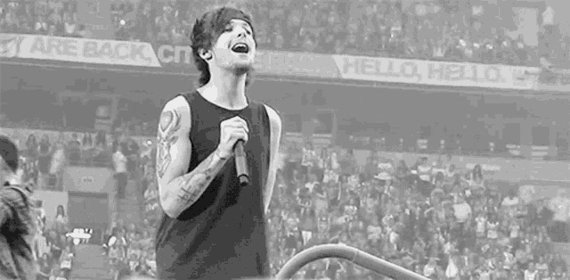 a black and white photo of a man singing into a microphone in front of a crowd .