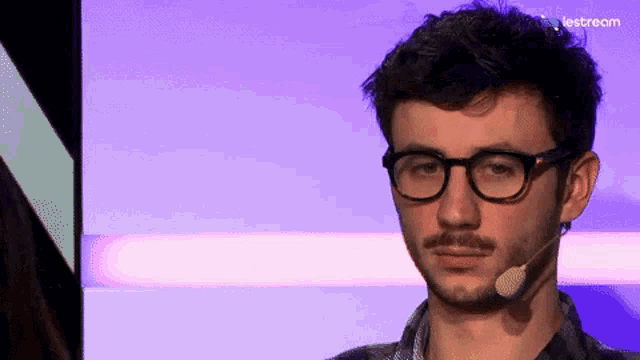 a man wearing glasses and a microphone stands in front of a purple background that says lestream