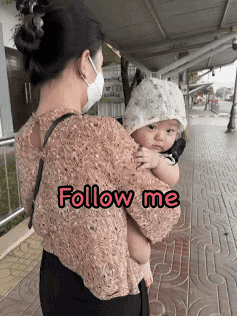 a woman wearing a face mask is holding a baby and the words follow me are above her