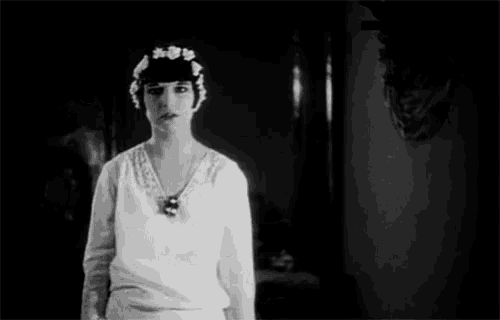 a black and white photo of a woman in a white dress and a flower crown on her head .