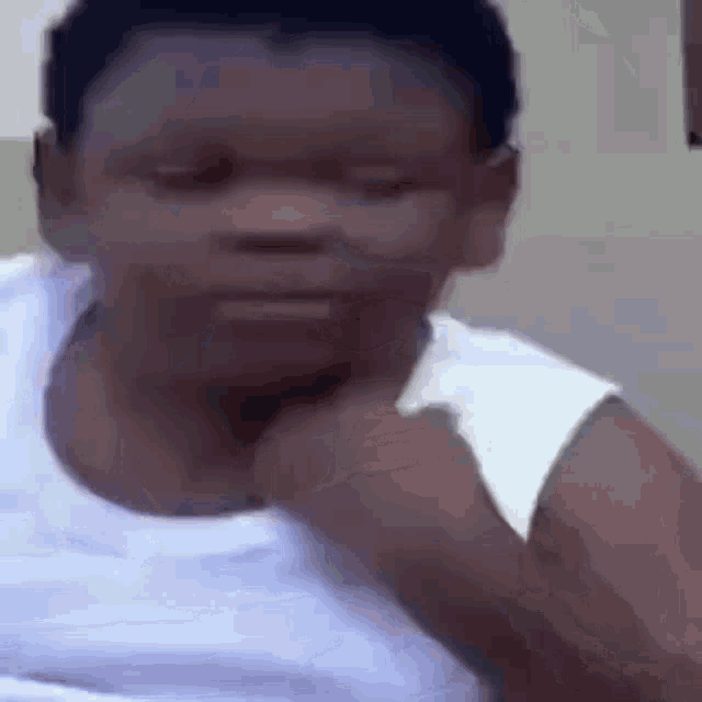 a young boy in a white tank top is making a funny face while holding his hand to his chin .