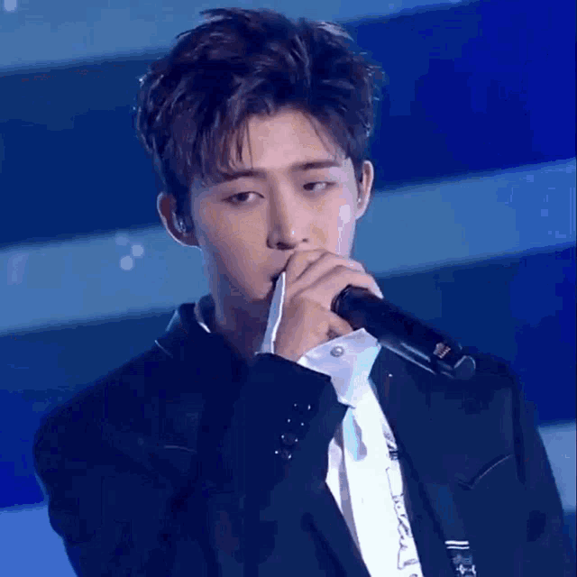 a young man singing into a microphone with a blue background
