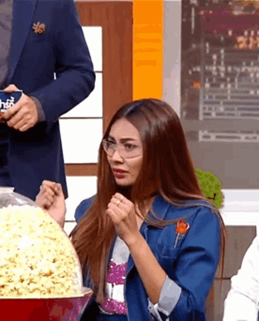 a woman wearing glasses is sitting in front of a bowl of popcorn ..