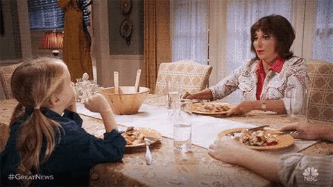 a little girl is sitting at a table with plates of food and a woman .