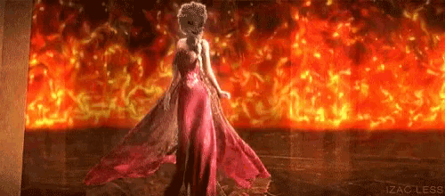 a woman in a long red dress is standing in front of a wall of fire .