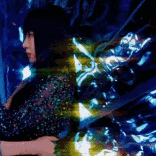 a woman in a sequined dress is standing in a dark room with a blue background .