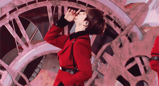 a man in a red jacket stands in front of a clock with roman numerals vii and xii