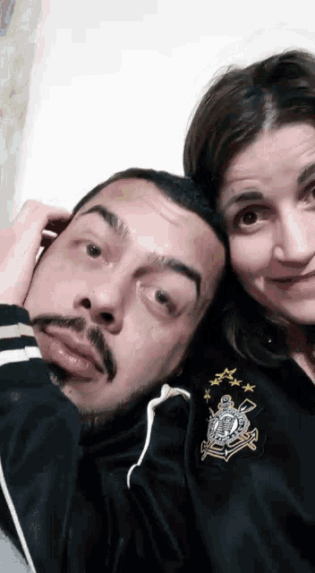 a man and a woman are posing for a picture and the man is wearing a black jacket with a shield on it