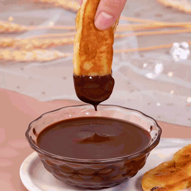 a person dipping a donut in chocolate sauce