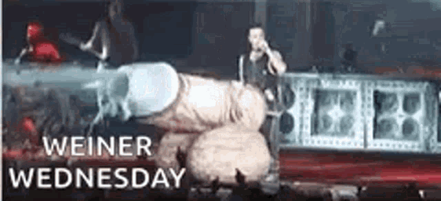 a man is standing on a stage with a microphone in his hand and the words weiner wednesday written on the bottom .