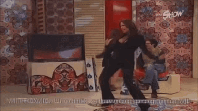 a woman in a black suit is dancing in front of a tv screen that says show