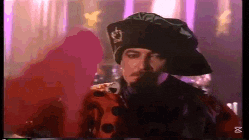 a man wearing a hat with a crown on it is standing in front of a purple wall