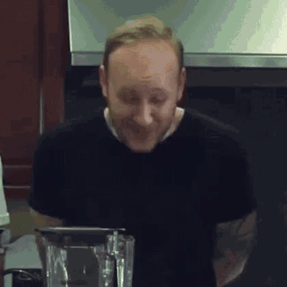 a man in a black shirt is making a funny face while using a blender in a kitchen .