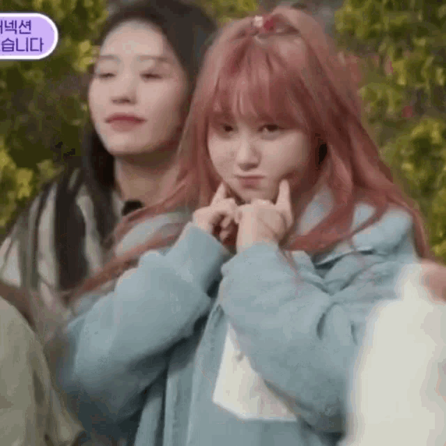 a girl with pink hair is making a funny face while another girl looks on .