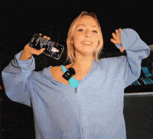 a woman in a blue jacket is holding a cell phone that says ' spotify ' on it