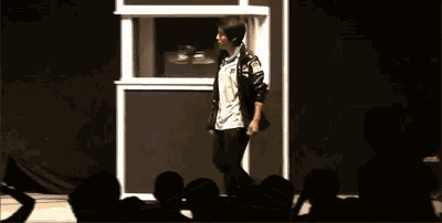 a man in a black jacket walks on a stage