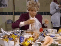 a woman is sitting at a table with a lot of food and eating a hamburger .