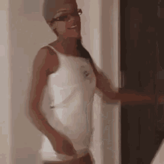a woman wearing glasses and a white tank top is standing in a room .