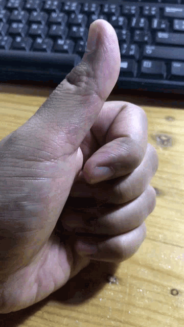 a close up of a person 's hand giving a thumbs up in front of a keyboard
