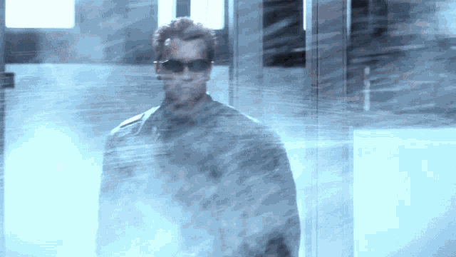 a man wearing sunglasses stands in a foggy room with the letter h visible