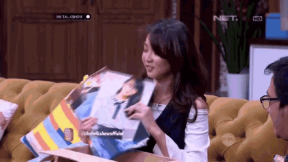 a woman is sitting on a couch holding a pillow with a picture of a man on it and the word net on the screen