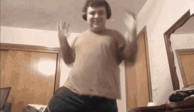 a man wearing headphones and a brown shirt is dancing in a room