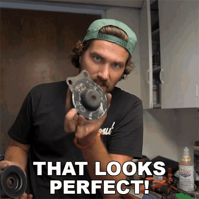 a man in a green hat is holding a piece of metal and says " that looks perfect "