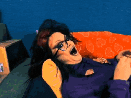 a woman wearing glasses and a lakers shirt is laying on a couch with her mouth open