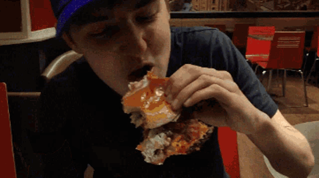 a man wearing a blue hat is eating a piece of pizza