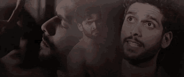 a shirtless man with a beard is looking up at something .
